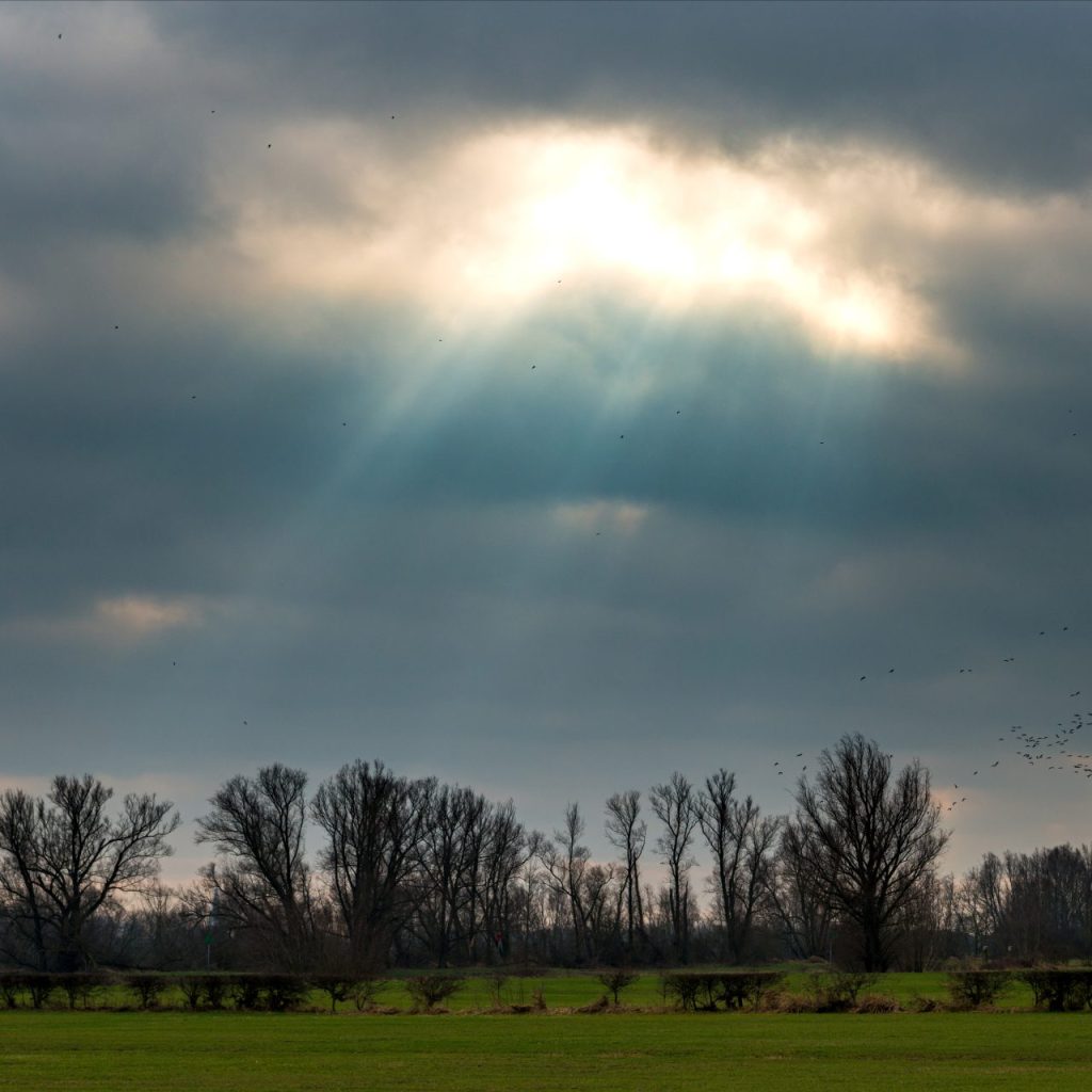 Sun shining through dark clouds over a green field